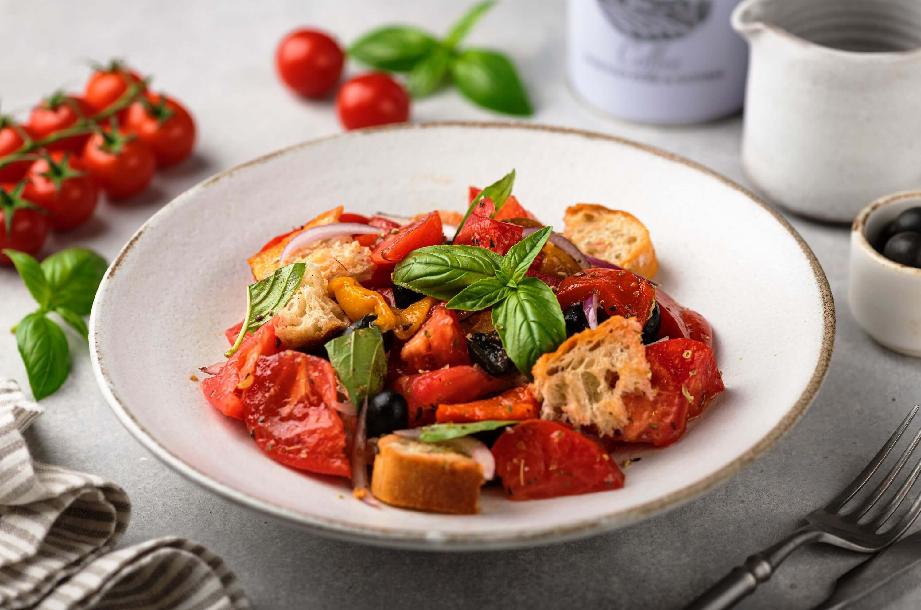 Frischer mediterraner Brotsalat mit Tomaten, Oliven und Basilikum, serviert als Beilage zum Grillen.