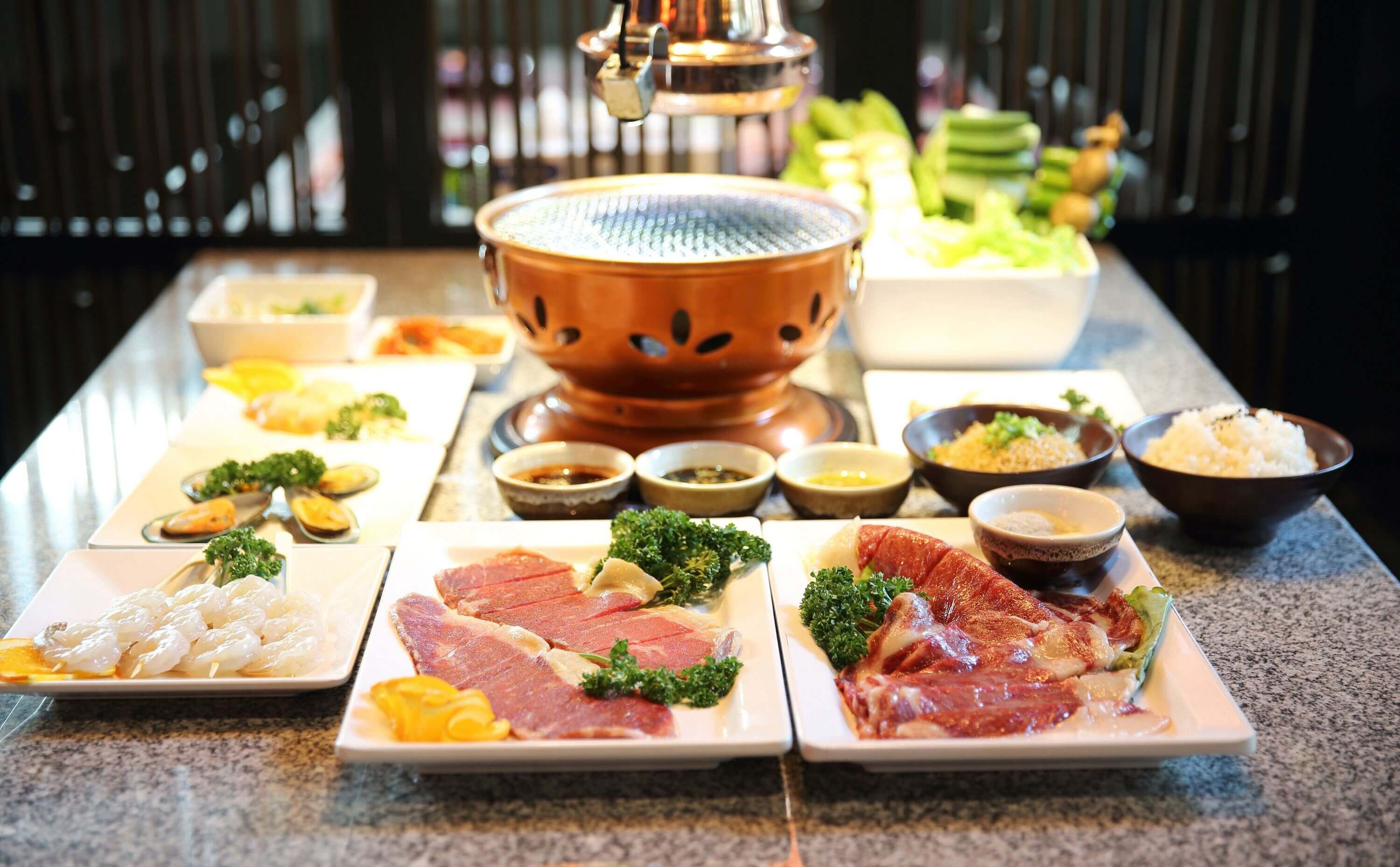 Traditioneller japanischer Tischgrill für Yakiniku mit verschiedenen rohen Zutaten wie Fleisch, Meeresfrüchten und Soßen, die für das BBQ bereit sind.