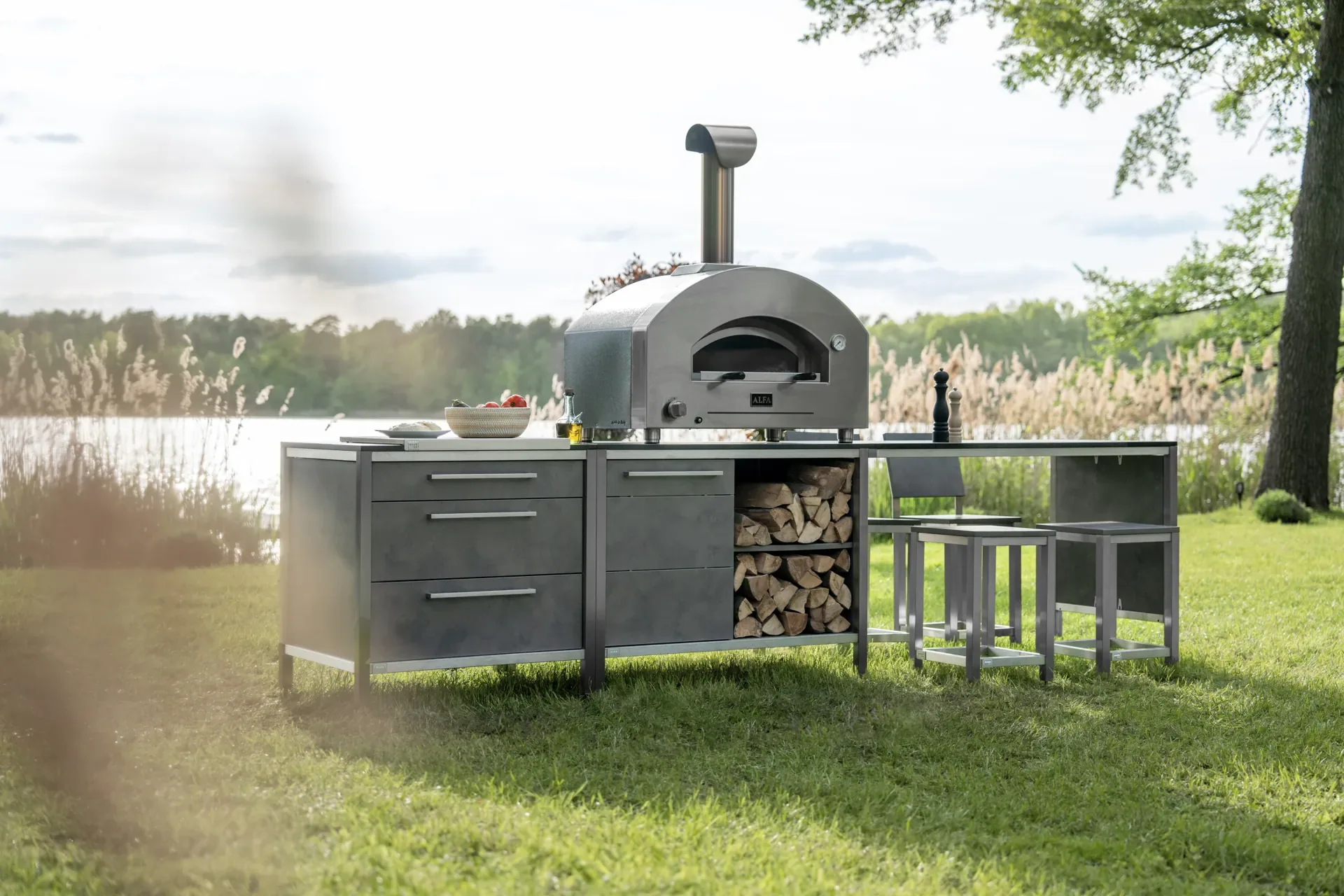 Pizzaofen auf einem Wagen mit Brennholzfach im Garten