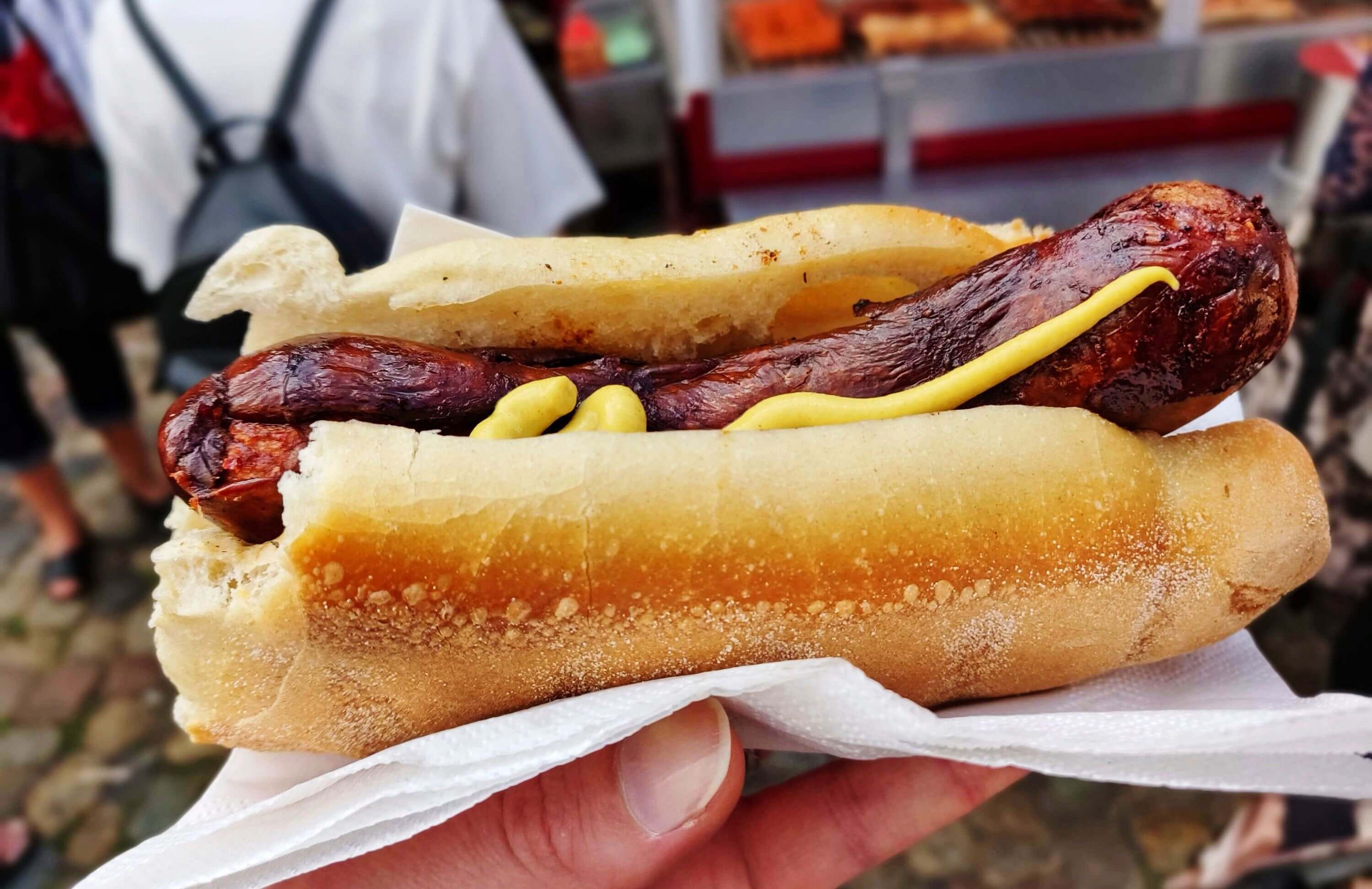 Bratwurst in einem Brötchen mit Senf, in der Hand gehalten.