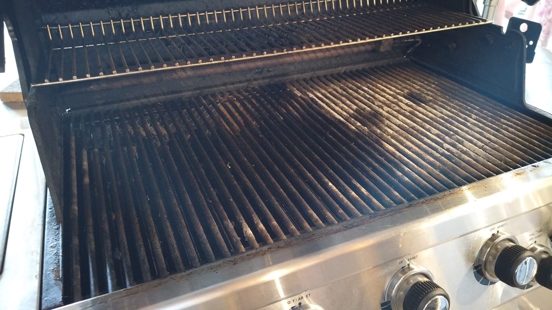 Stark verschmutzter Gasgrill mit eingebrannten Fettrückständen auf dem Grillrost vor der Reinigung