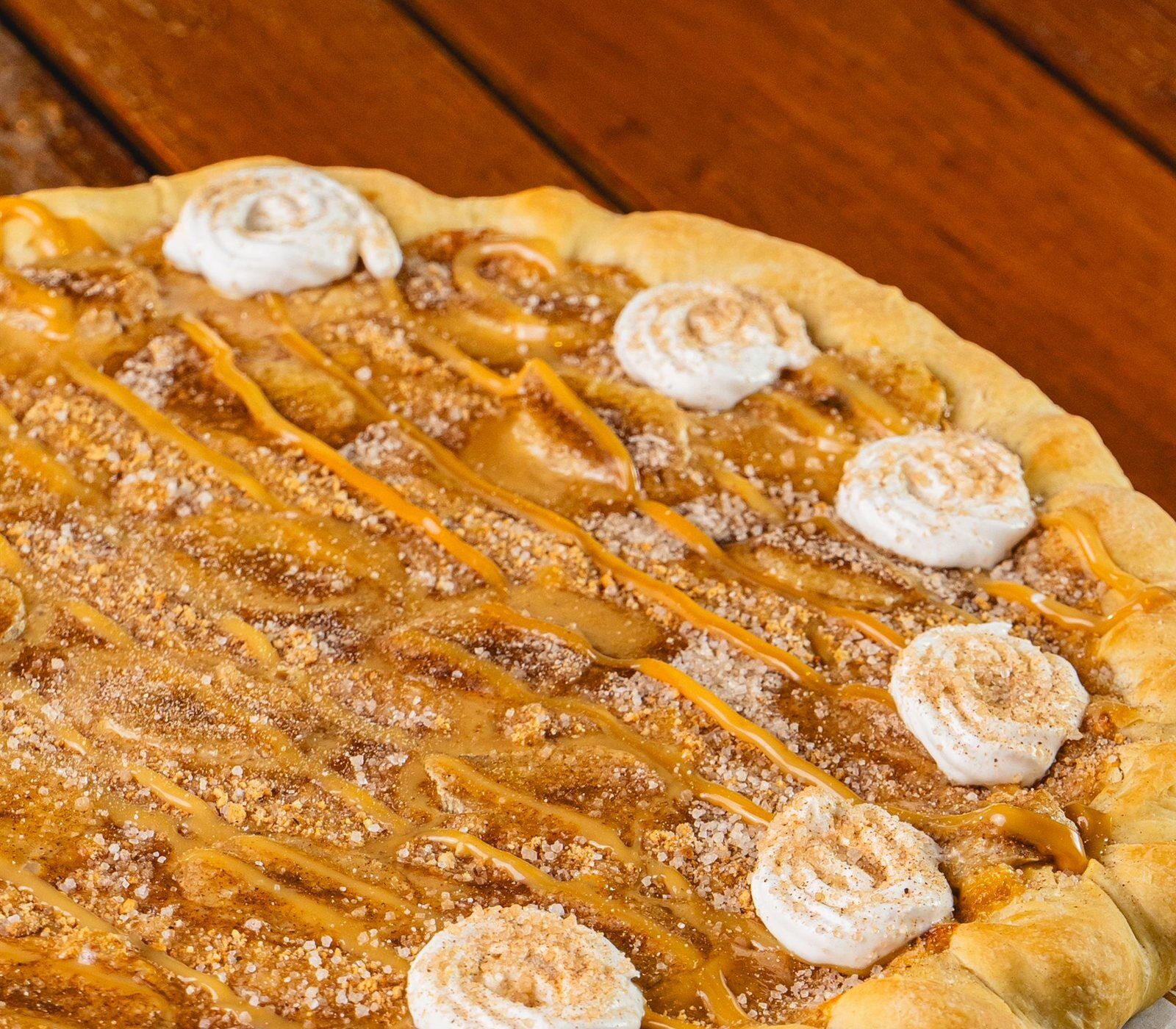 Süße Pizza mit Vanillepudding, Biscoff-Creme und Keks-Crumble auf einem Holztisch
