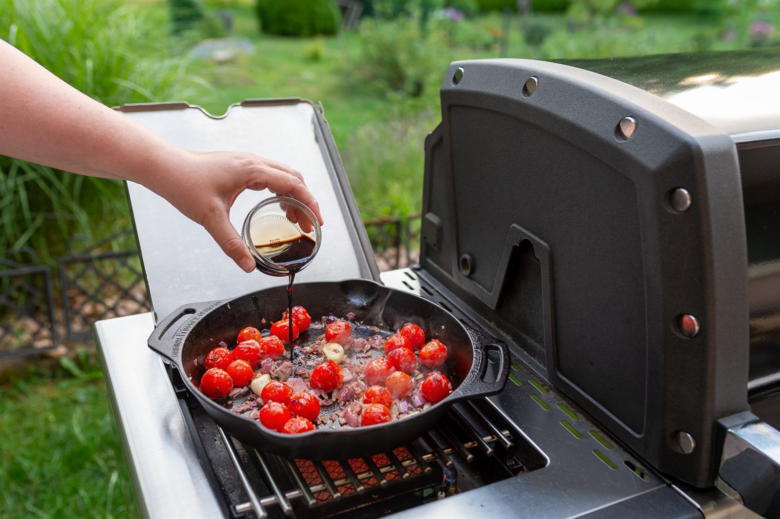 Cherrytomaten und rote Zwiebeln in der Gusspfanne werden mit dunklem Balsamico abgeloescht