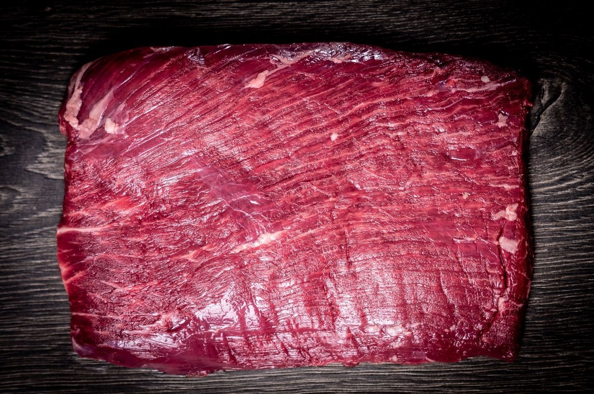 Rohes Flanksteak vom Rind auf dunklem Holz, die langen Fasern laufen quer über das ganze Stück