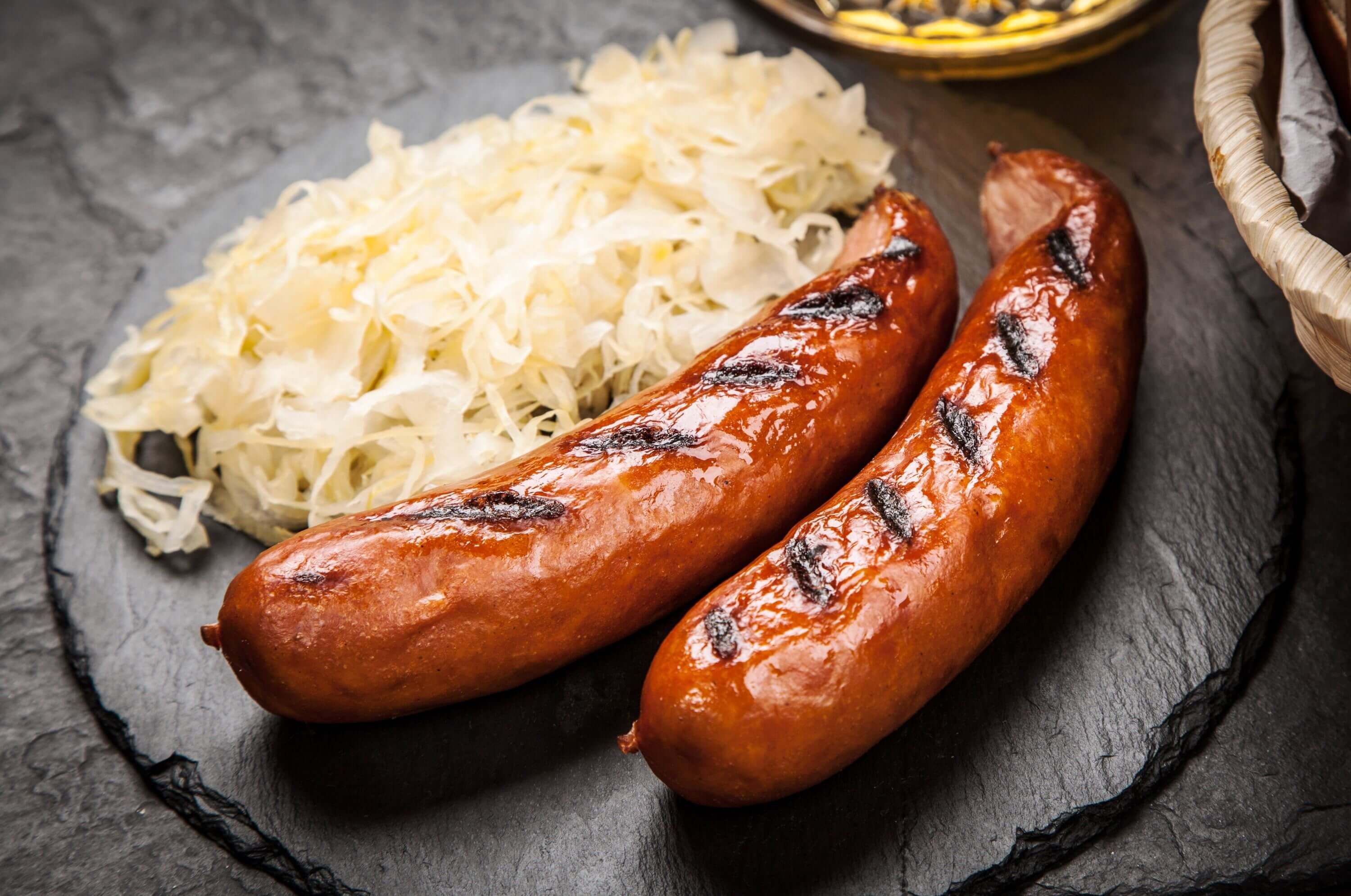 Gegrillte Bratwurst mit Sauerkraut auf einem Schieferbrett serviert.