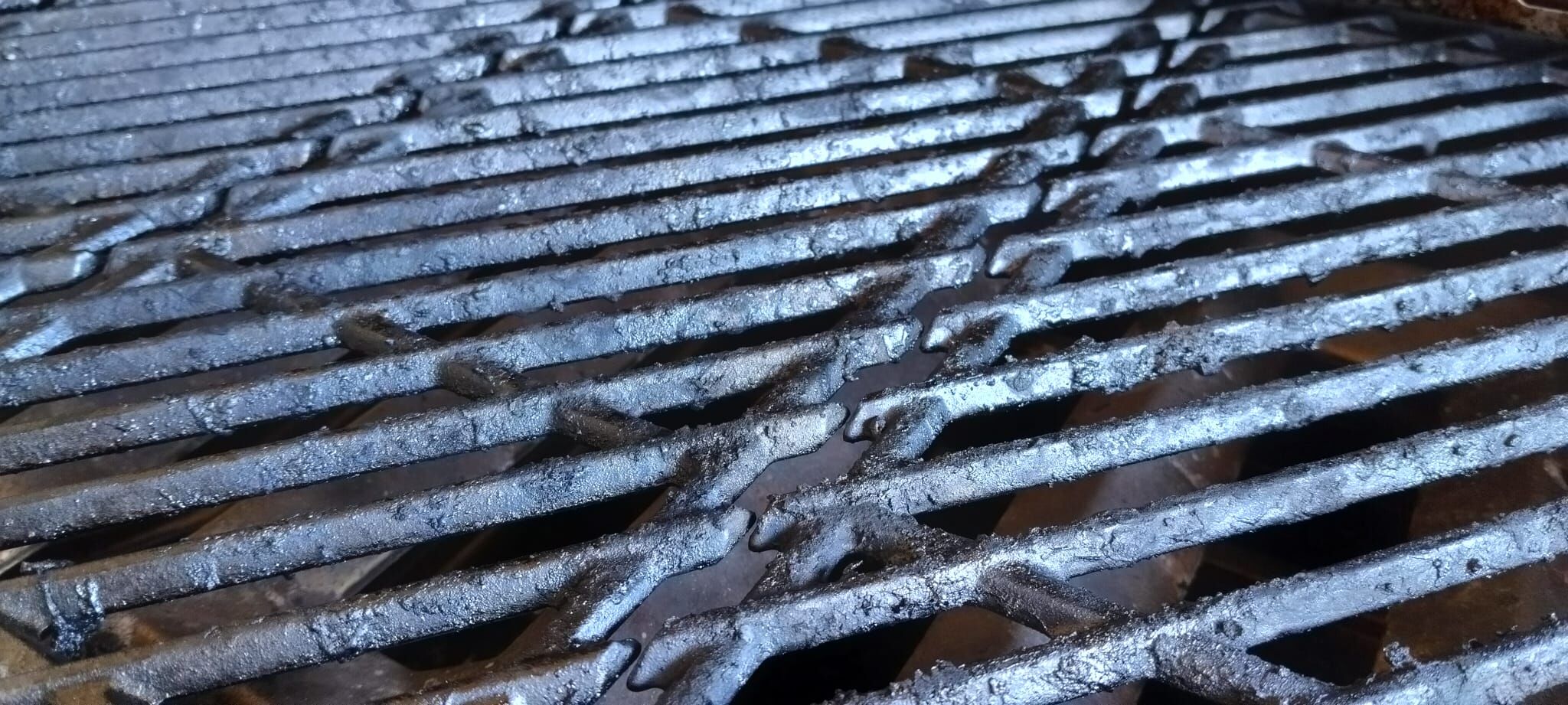 Verkrusteter Grillrost eines Gasgrills mit hartnäckigen Fettrückständen vor dem Ausbrennen