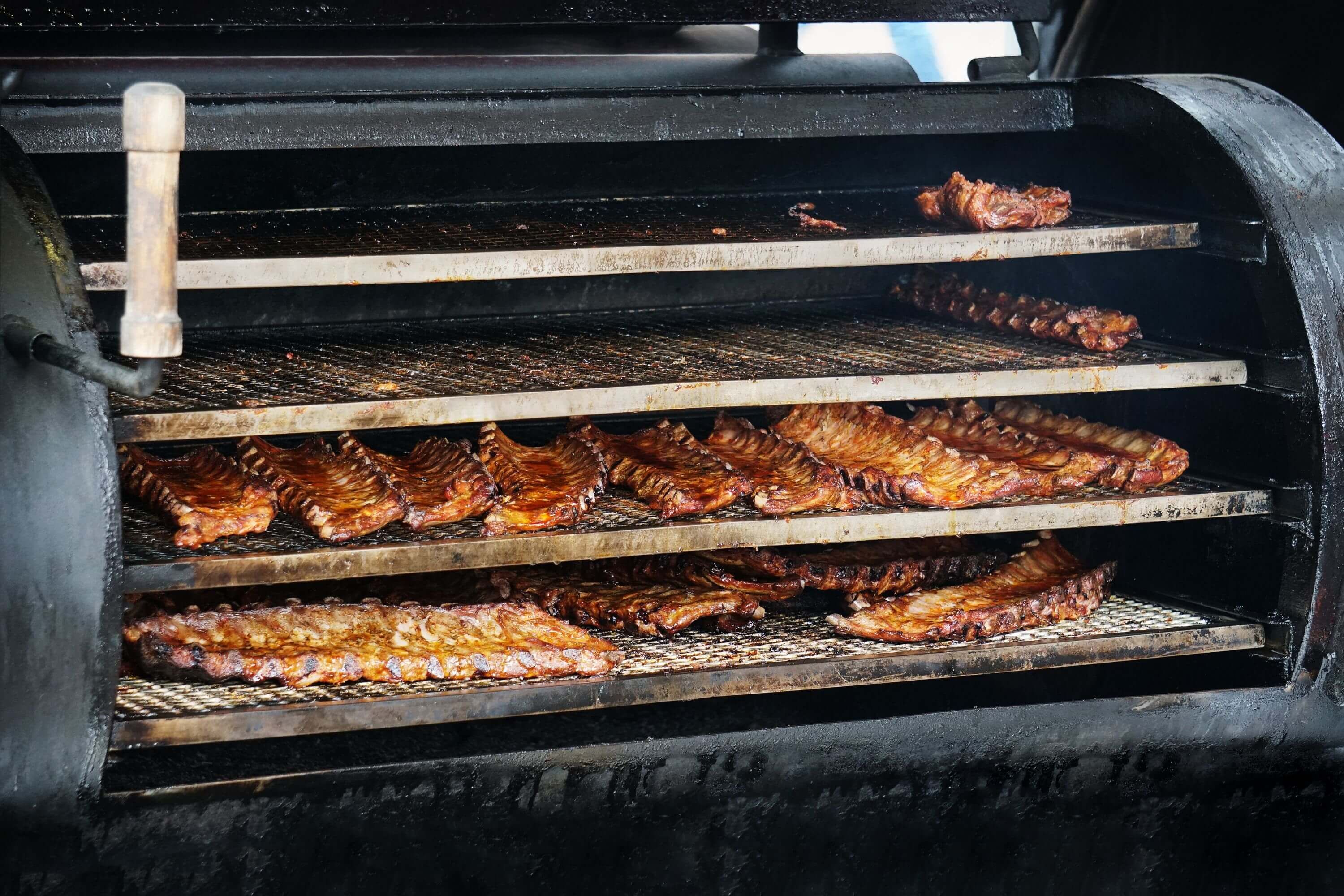 Viele Ribs und Spareribs auf dem Barbecue Smoker im Rauch