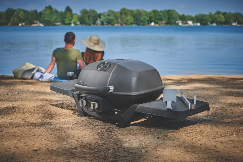 Napoleon TravelQ PRO 285 im Sand am Seeufer, dahinter ein Paar auf einer Decke