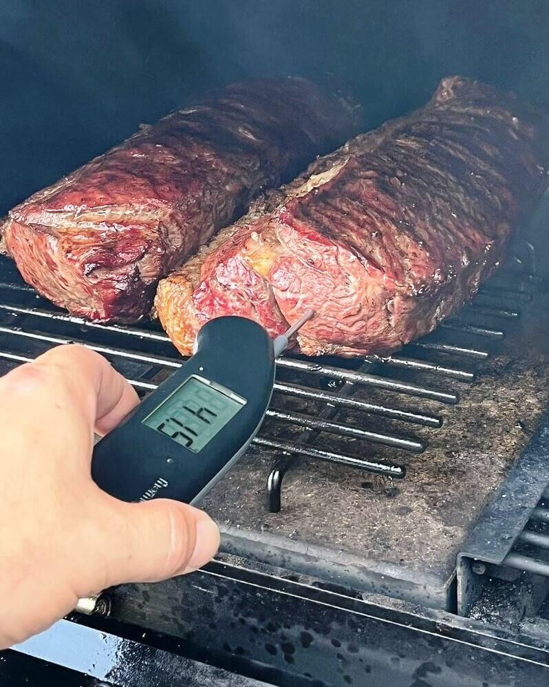 Mit einem Einstichthermometer wird die Kerntemperatur von Fleisch auf dem Rost gemessen