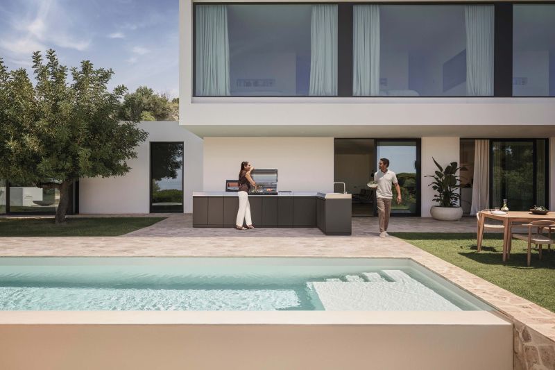 Paar an einer Miele Dreams Outdoorküche vor einer modernen Villa mit Pool