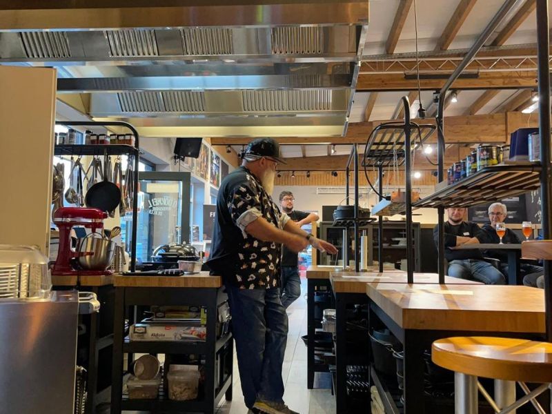 Ein Kursleiter erklärt in der Grillschule, im Hintergrund hören Teilnehmende zu